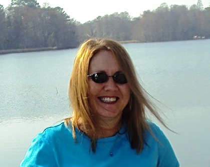Debbie smiling, with a sprawling lake behind her.