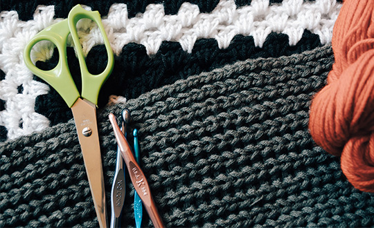 Close-up of a crochet project, gray yarn, with scissors and crochet needles.