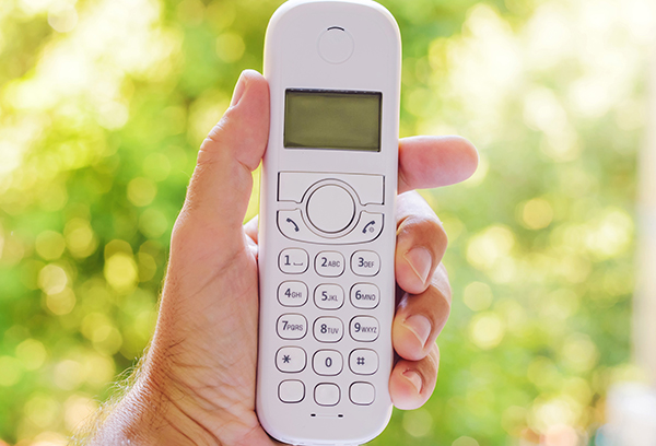 Hand holding a white cordless telephone with buttons.